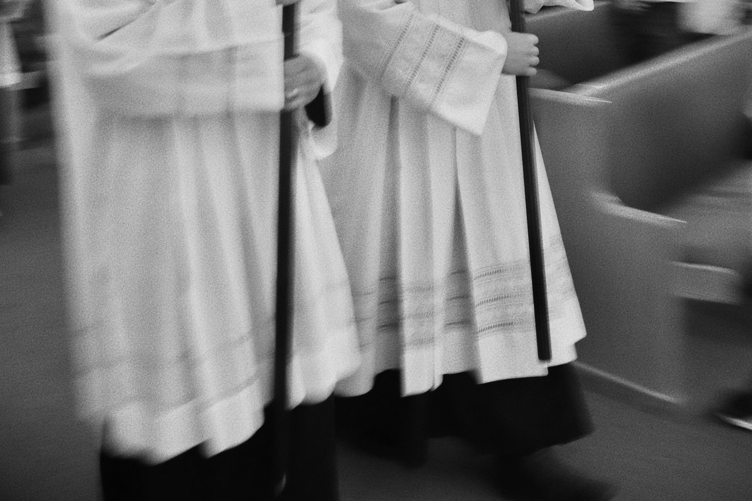 Motion-blurred black and white photo of  altar server surplices swaying during movement.