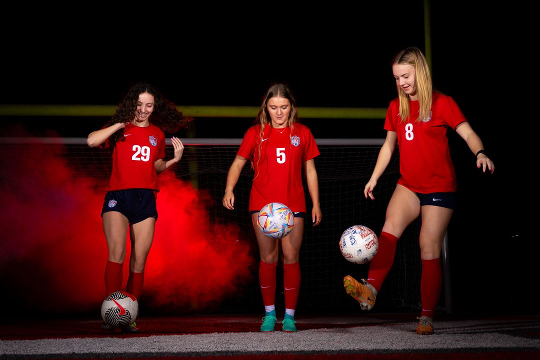 Soccer players in red jerseys pose with soccer balls for a dramatic team photo.
