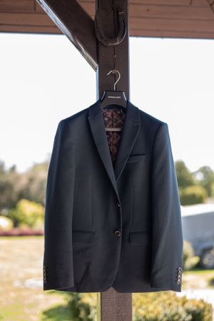A classic navy suit jacket hanging on a wooden hanger outdoors.