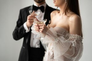 Close-up of champagne glasses held by a couple in formal wedding attire.