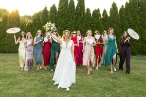 Wedding party celebrating on a grassy lawn at sunset with parasols and colorful dresses.
