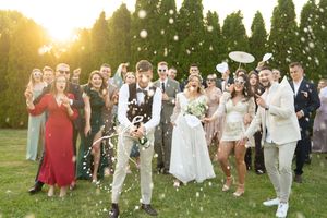Large wedding party celebrates outdoors with confetti throws against a backdrop of evergreen trees.