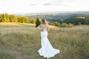 Bride in flowing white dress twirls across scenic mountain meadow at sunset.