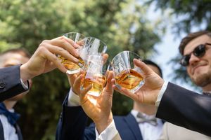 Wedding party toasting with glasses of whiskey outdoors in celebratory moment at sunset.