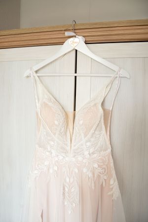A delicate white wedding dress with lace details hanging on a custom hanger.