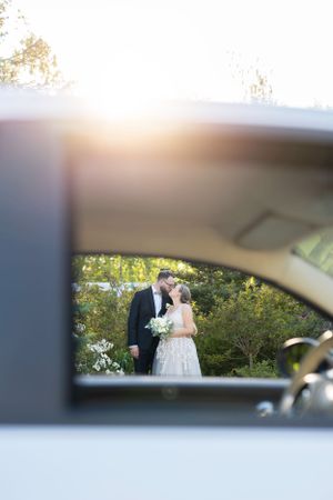 A wedding couple captured through a car side mirror in a garden setting.