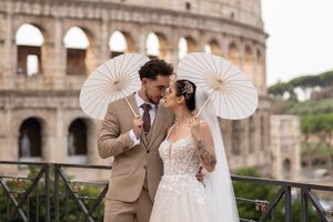 A romantic wedding couple poses with parasols in front of the historic Colosseum in Rome, Italy.