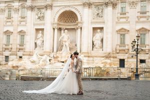 A couple shares a romantic moment in front of an ornate European palace with classical architecture and stone sculptures.