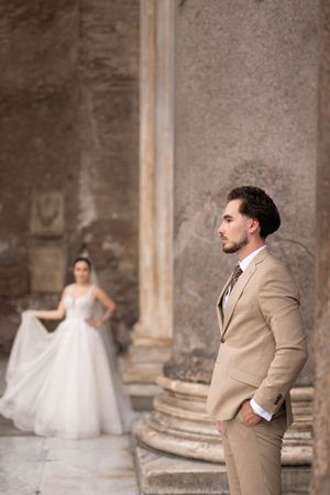 Wedding couple poses dramatically in front of stone columns in a series of artistic first look photos.