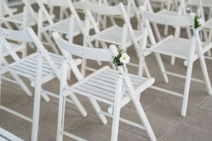 White folding chairs with single flower decorations arranged for outdoor wedding ceremony.