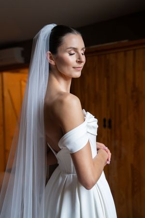 A bride in a white off-shoulder wedding dress and veil poses gracefully in a series of profile shots.