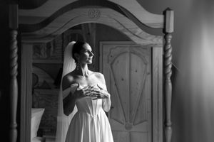 A dramatic black and white portrait of a bride in a flowing white gown standing in an ornate doorway.