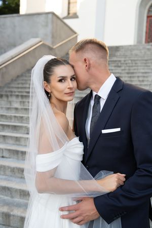 Romantic wedding couple sharing intimate moments on elegant stone steps in formal attire.