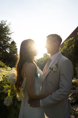 A romantic sunset silhouette of a bride and groom embracing in a garden setting with golden light streaming through the trees.