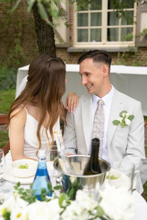 A couple sits at an elegant outdoor table setting with blue and clear glassware and white floral decorations.