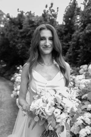 A series of black and white photos showing someone in a white dress holding a beautiful floral bouquet in a garden setting.