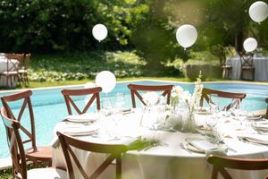 Elegant outdoor wedding reception tables set with white linens and floral centerpieces beside a swimming pool.