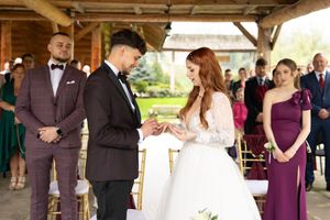 Wedding party members in purple dresses and dark suits pose together during an outdoor celebration.