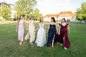 Bride and four bridesmaids in colorful gowns walk hand-in-hand across a green lawn at an outdoor wedding venue.