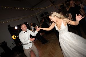 Bride and groom dancing energetically at wedding reception with string lights in background.