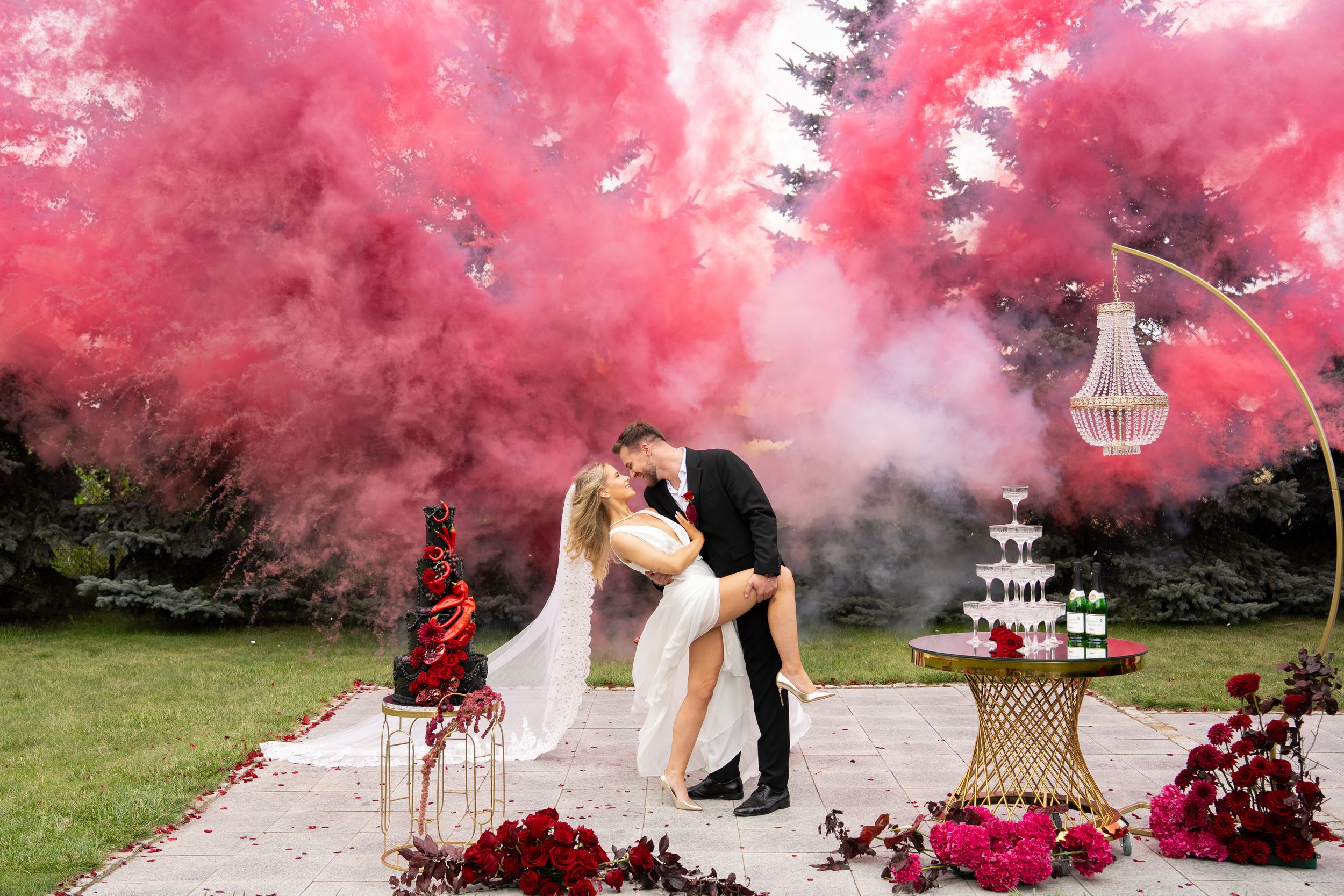 Couple embraces in a dreamy outdoor setting surrounded by vibrant pink smoke bombs creating a romantic atmosphere.