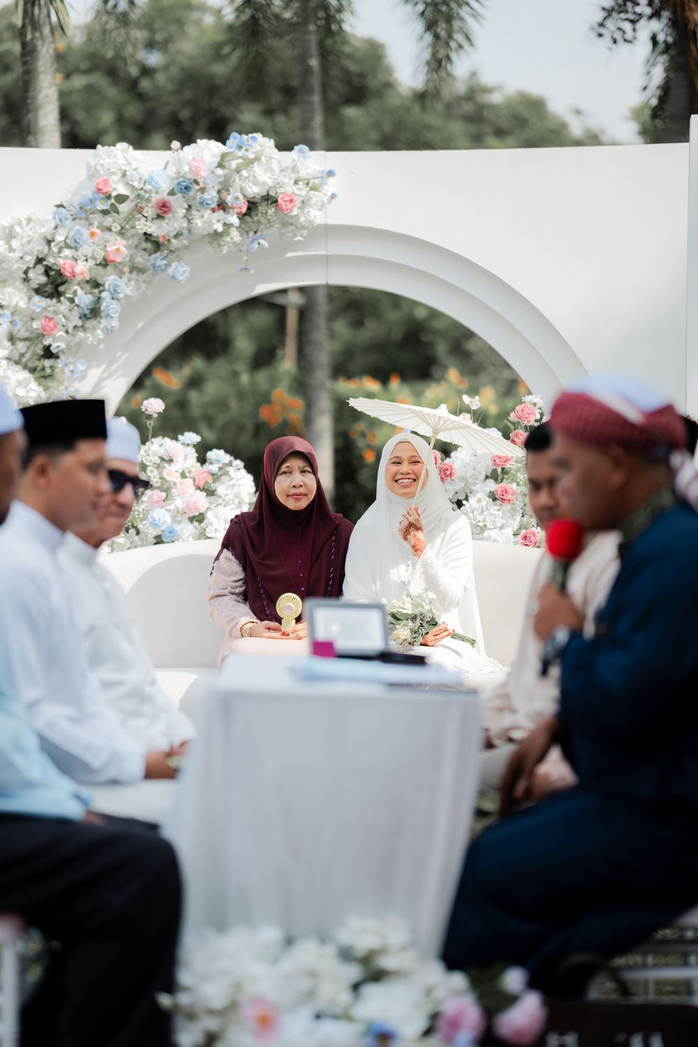 Outdoor wedding ceremony setup with white arch adorned with pink florals and intimate seating arrangement.