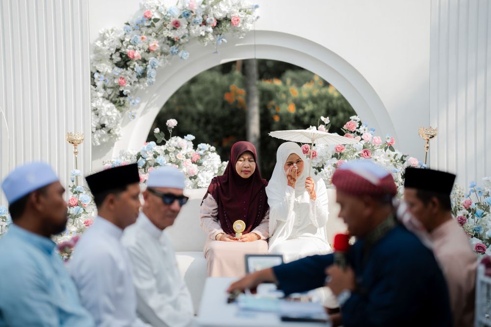 Intimate outdoor wedding ceremony gathering under white floral arch with traditional cultural elements.