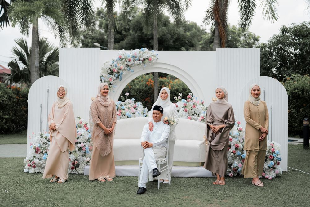 Wedding party posed formally under white floral arch with coordinated neutral-toned attire.