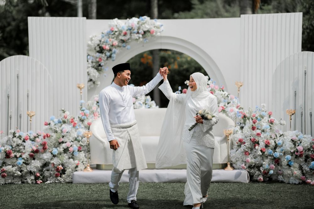 Joyful couple celebrates during their wedding ceremony under a beautiful floral arch with pink and white blooms.