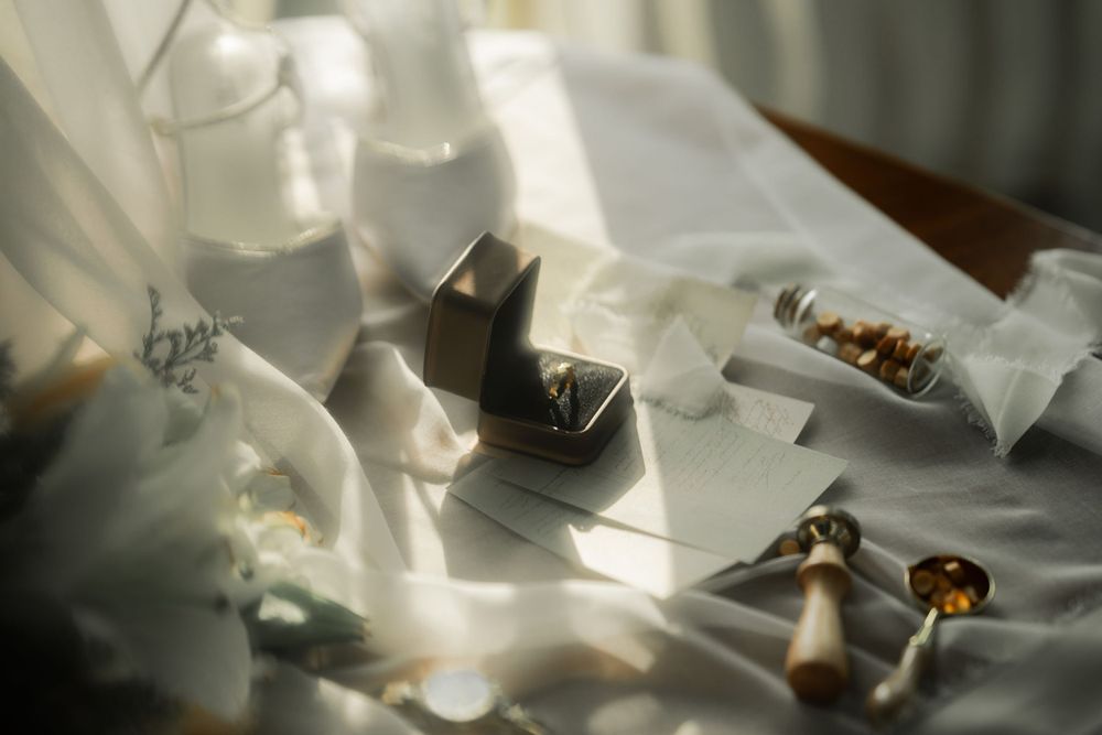 Wedding rings and jewelry boxes artistically arranged on white fabric with soft natural lighting.
