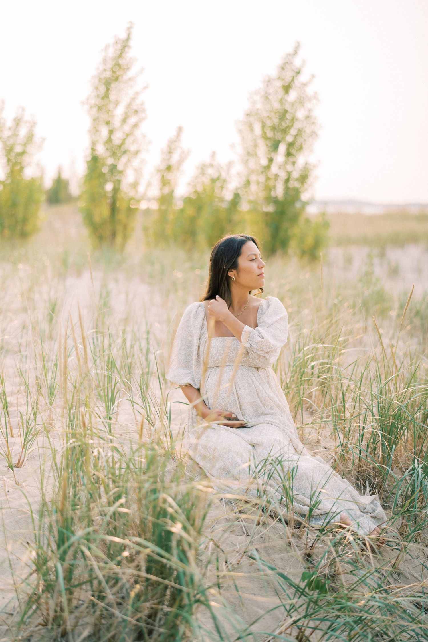 An ethereal maternity photo shoot in a field of tall grass at golden hour.
