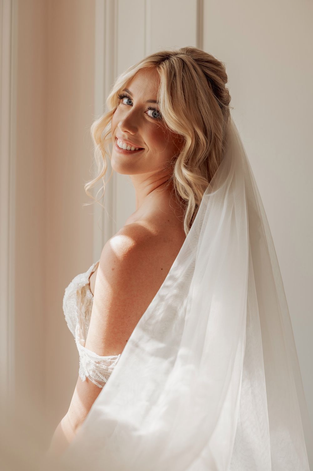 A bridal boudoir photo series showing ethereal poses in soft natural window light with flowing white fabric and veil.