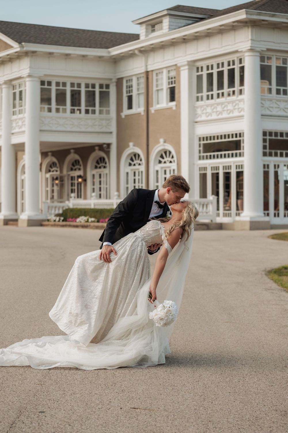 A romantic wedding couple shares a dip pose in front of a grand white columned building.