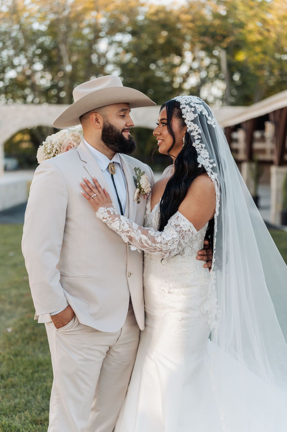 A romantic wedding couple in all white attire embracing outdoors during golden hour.