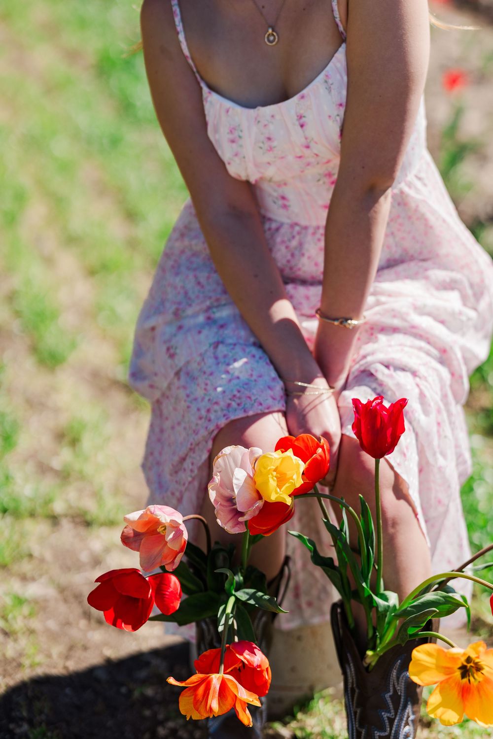 Person in a floral dress sitting with colorful tulips and poppies in a garden setting.
