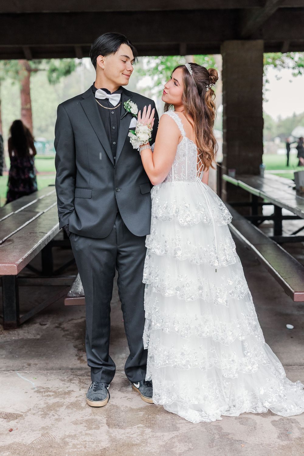Newlyweds pose together on rustic picnic benches, with bride in layered lace gown and groom in classic black suit.