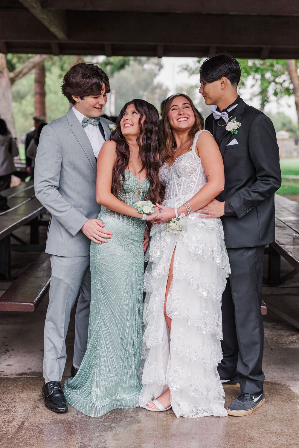 Two couples in elegant formal attire pose together at prom, wearing suits and flowing dresses in mint green and white.