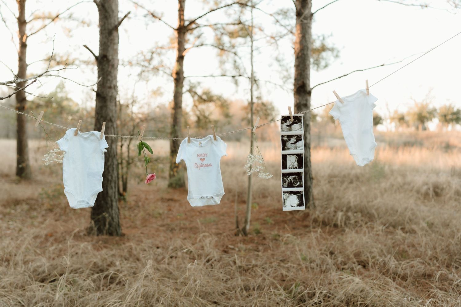 Baby clothes hanging on clothesline between trees in rustic outdoor setting.