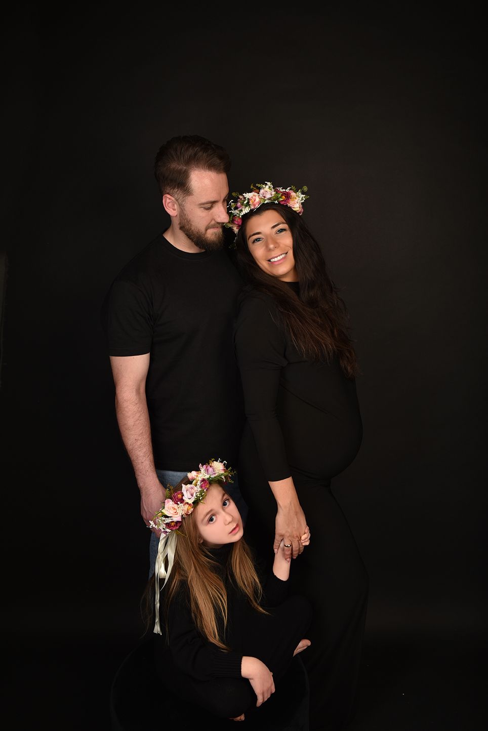 Familienfotografie, Family portrait in black clothing with floral crowns against dark background.