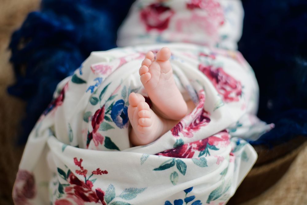 Tiny baby feet peek out from a floral patterned blanket against a dark blue background.