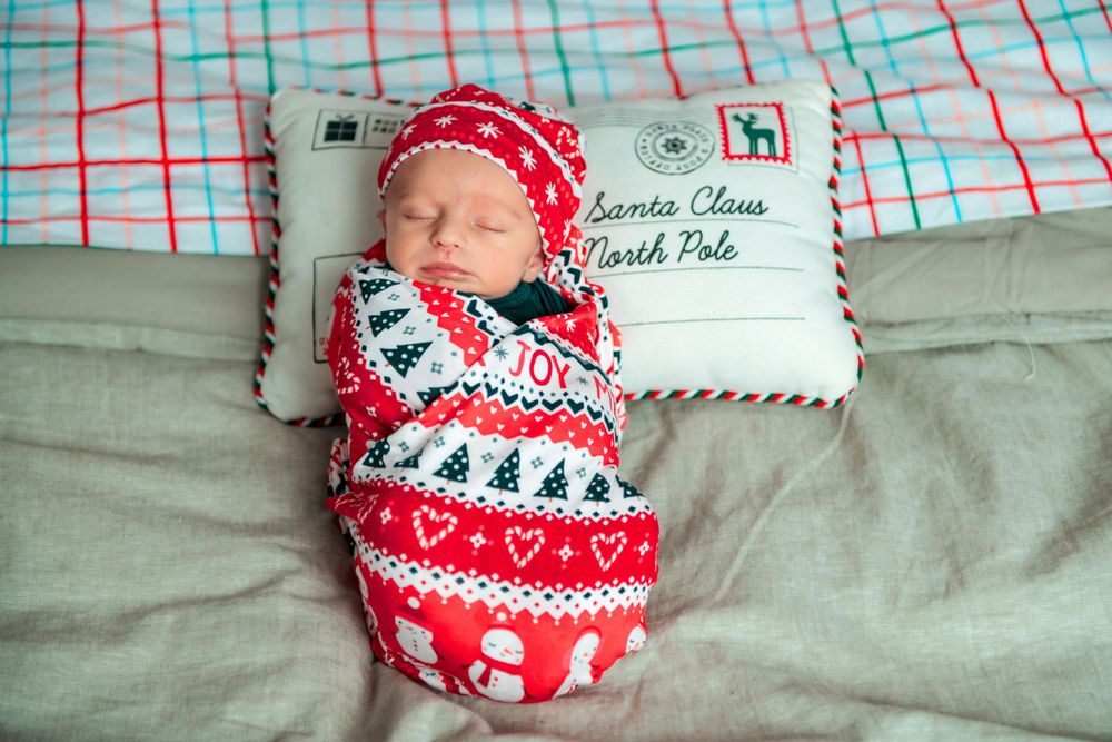 Newborn baby sleeping peacefully wrapped in red and white Nordic print Christmas swaddle with matching hat.