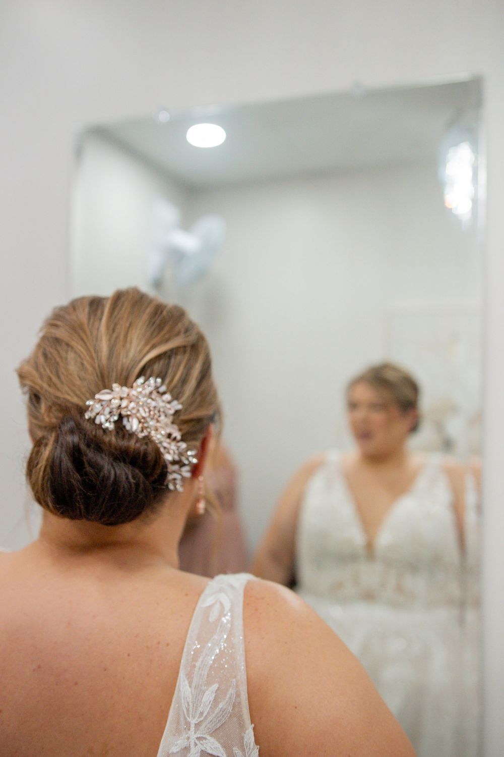 Bride in beaded wedding gown with elegant crystal hair comb updo, viewed from behind, reflected in a mirror.