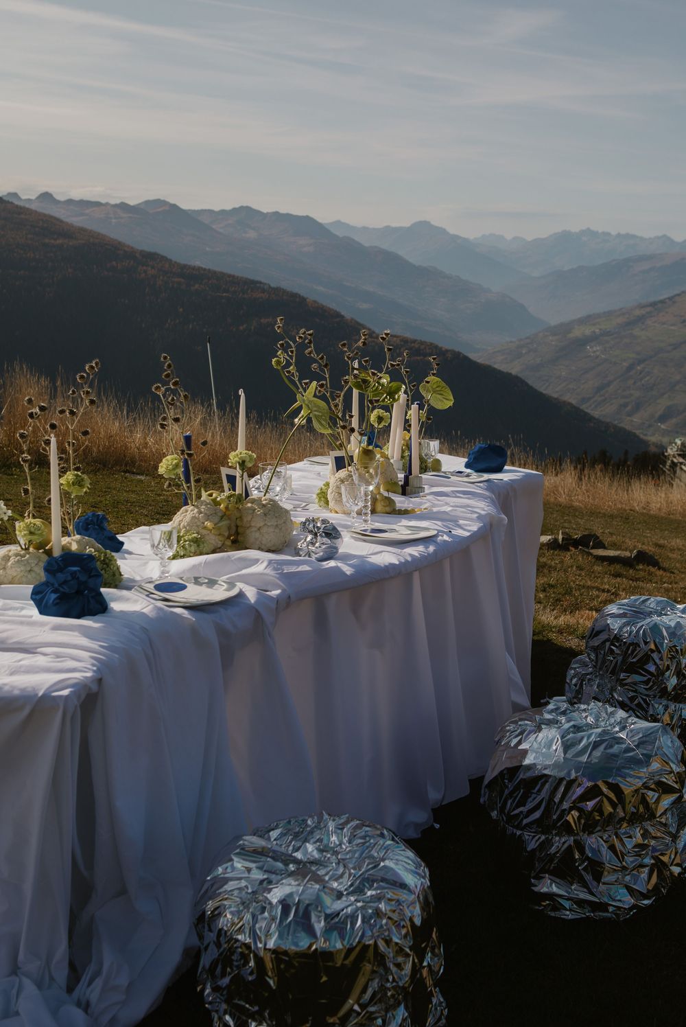 Elegant dining table set with white linens and place settings against a backdrop of majestic mountain peaks at sunset.