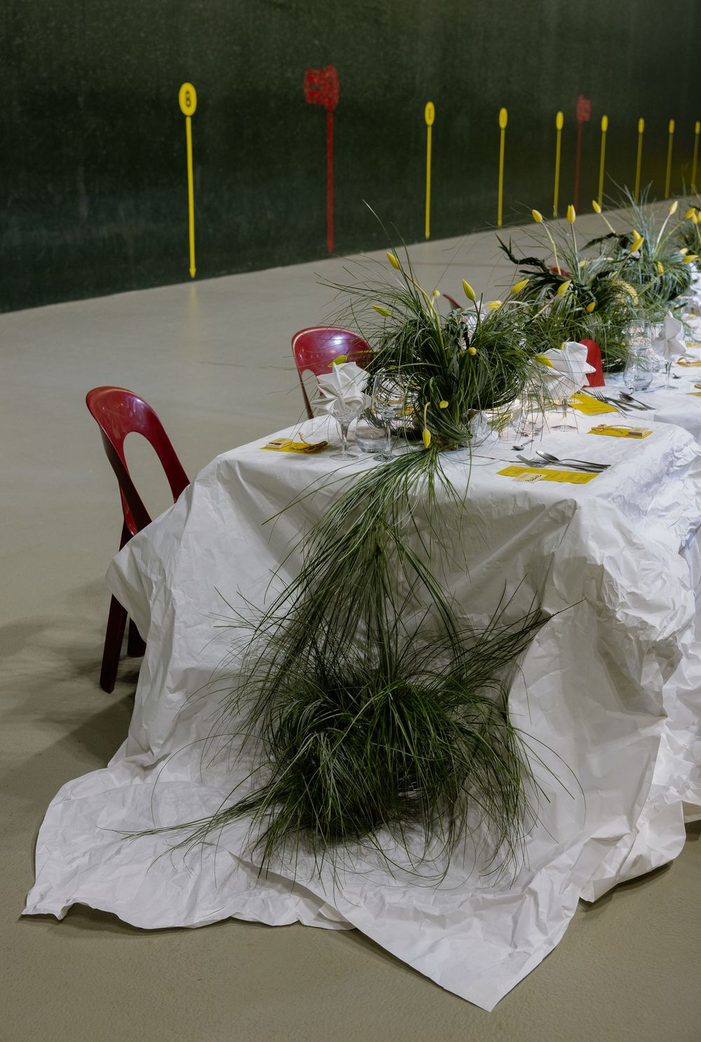 A series of white tablecloths with evergreen pine branch centerpieces and yellow and red accents set for a festive dinner.
