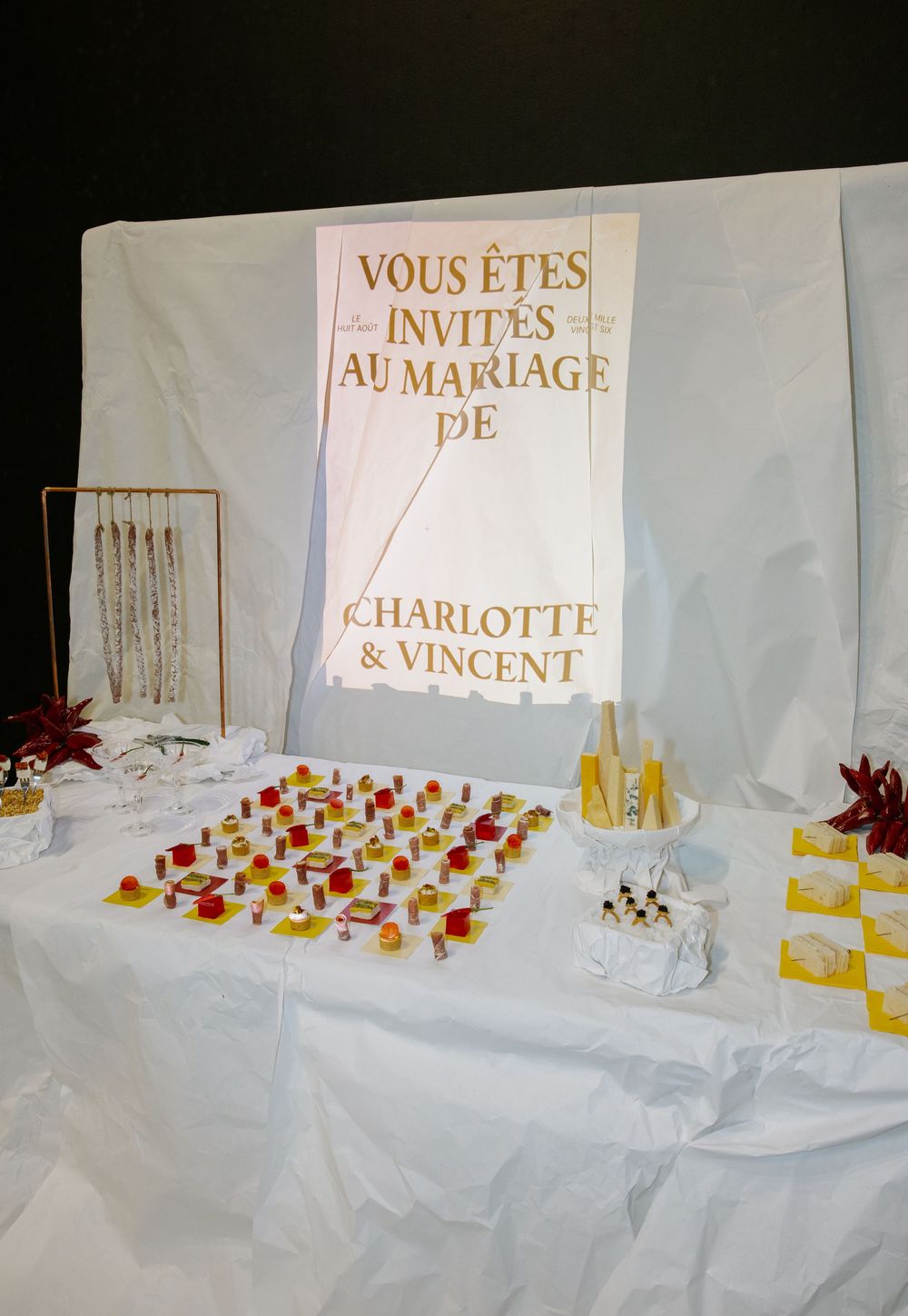 Wedding reception table setup with white linens, red and yellow decorative elements, and French invitation signage.