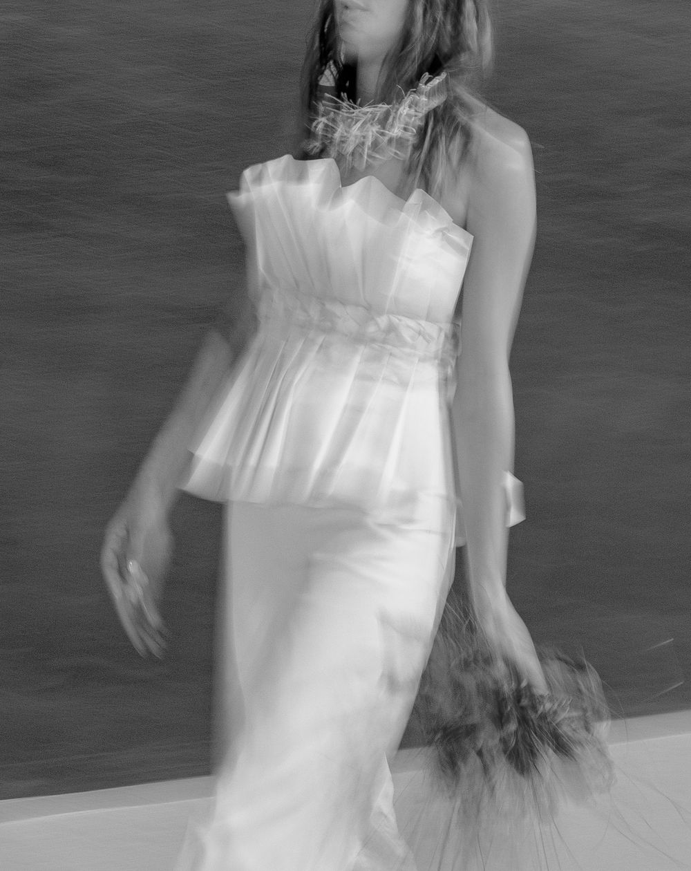 Black and white artistic photograph of someone in an elegant white wedding dress holding a bouquet with motion blur effect.