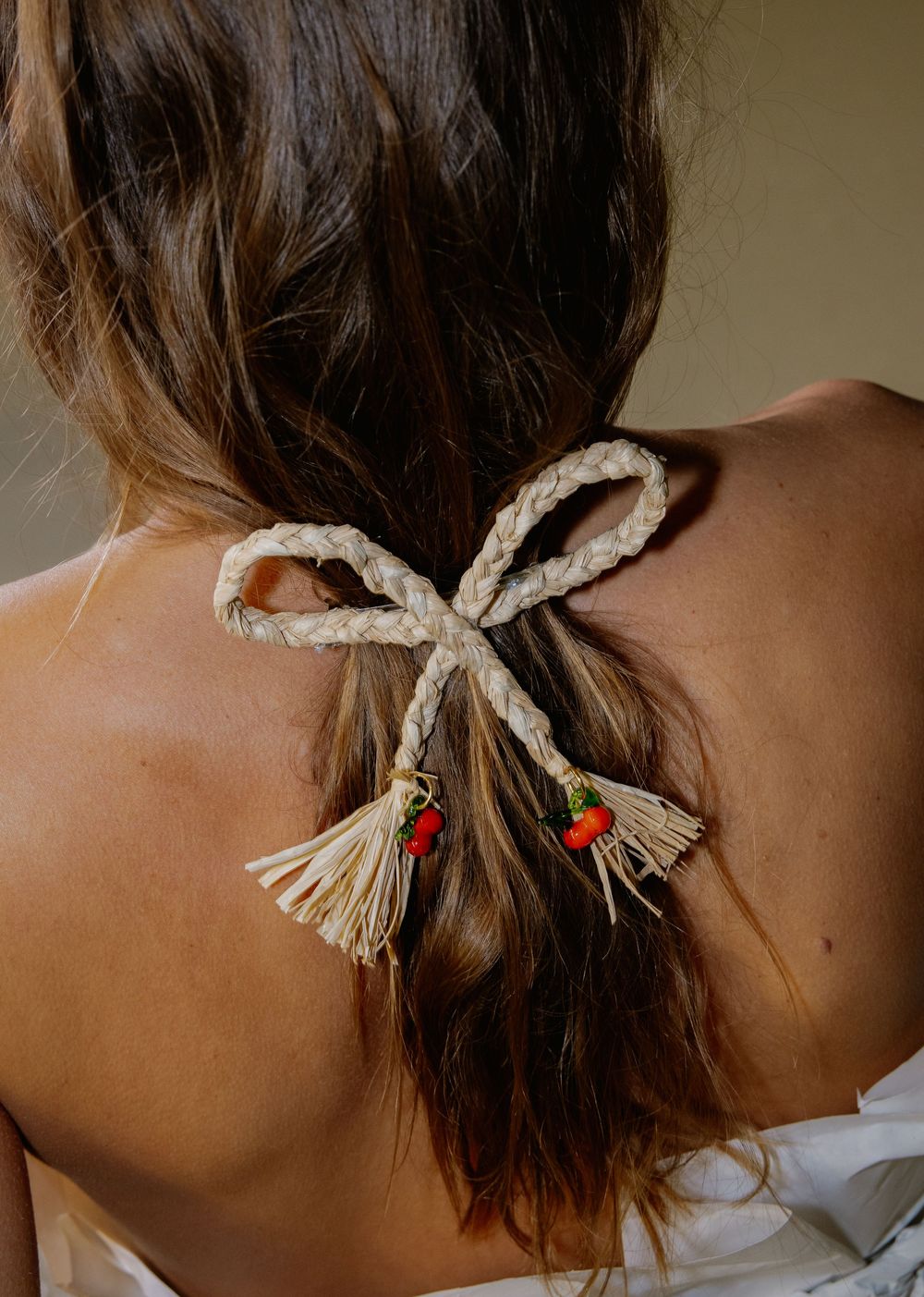A close-up sequence showing a rope being tied into a decorative bow on brown hair with red bead accents.