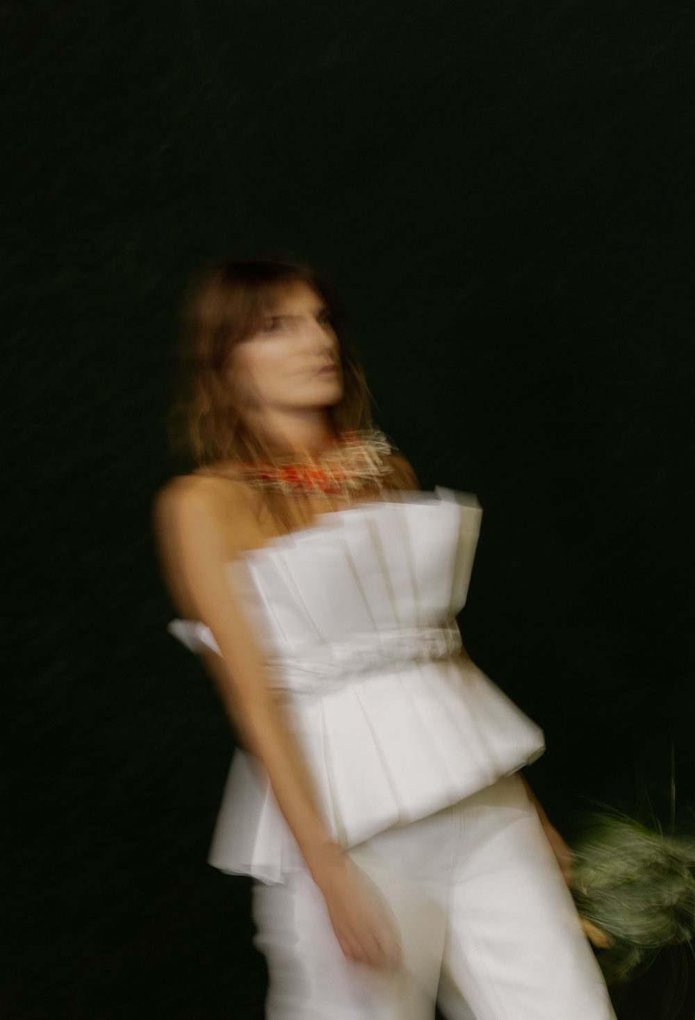 Artistic motion blur portrait of someone in a structured white outfit with ruffled details against a dark background.