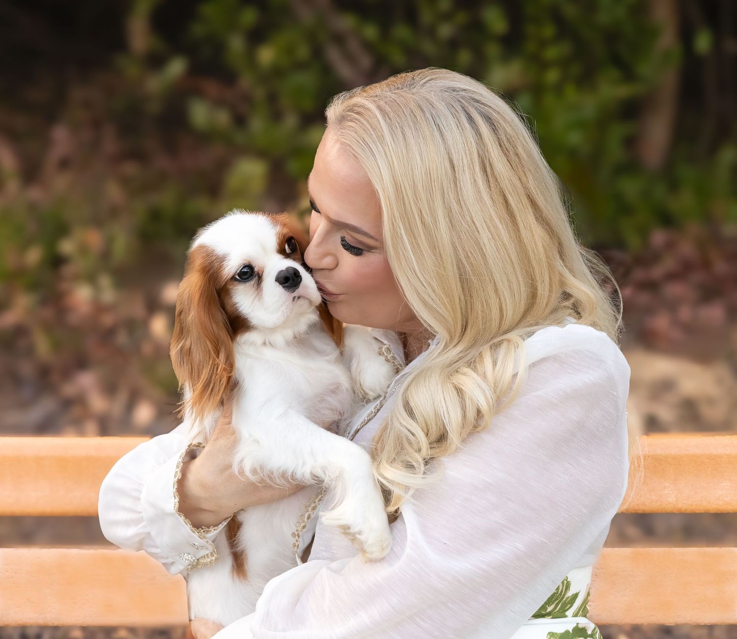 Sweet moment captured of person cuddling with Cavalier King Charles Spaniel puppy outdoors.