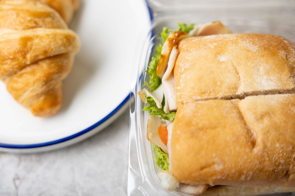 Fresh sandwich with lettuce and vegetables served on a white plate next to a flaky croissant.